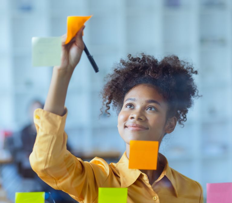 A project manager reviewing Post-It Notes on a glass wall